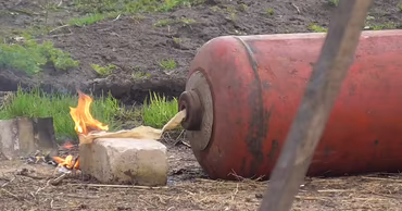 A red gas cylinder leaking gas and catching fire on the ground.