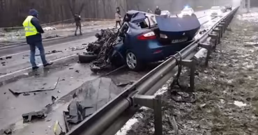 A severely damaged blue car at the scene of a road accident with emergency responders present.