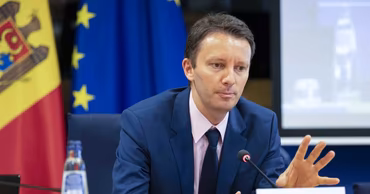 Siegfried Muresan speaking at a conference with Moldovan and EU flags in the background.