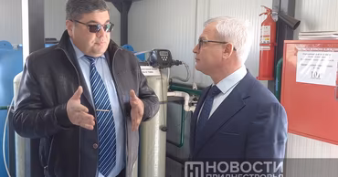Vitaly Nyagu in a suit and leather jacket talking to another official in a technical room.