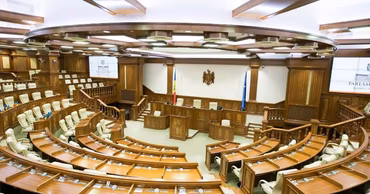 The interior of the Moldovan Parliament plenary hall with empty wooden desks and chairs.