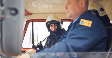 Two Moldovan firefighters in uniform sitting inside a fire truck.