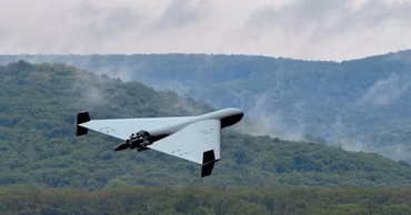 A military drone flying over a forested landscape.