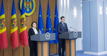 Marcel Spatari speaking at a press conference podium with Moldovan and EU flags in the background.