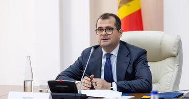 Vasile Tofan sitting at a conference table with a Moldovan flag in the background.