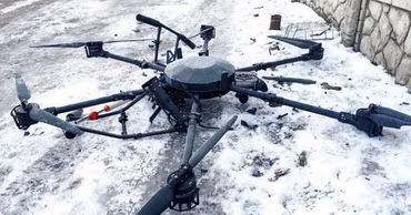 A crashed multi-rotor drone lying on snowy ground.