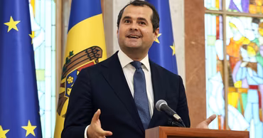 Vasile Tofan speaking at a podium with Moldovan and EU flags in the background.