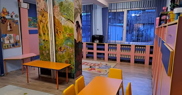 Interior of a colorful kindergarten classroom with tables, chairs, and wall paintings.