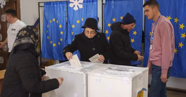 People casting ballots at a polling station with European Union flags in the background.