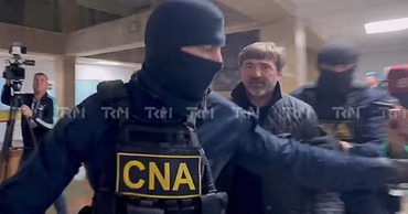 Vladimir Andronachi escorted by masked CNA officers in a hallway.