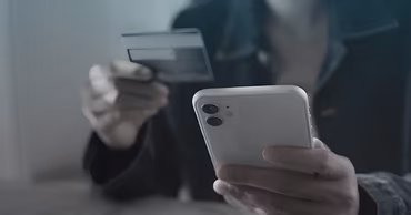 A person holding a smartphone and a bank card, representing online financial fraud.