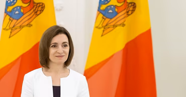 Moldovan President Maia Sandu standing in front of Moldovan flags.