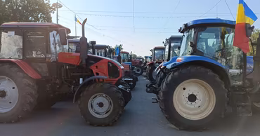 Several tractors parked in a row during a protest in Moldova with a Moldovan flag.