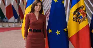 President Maia Sandu standing in front of Moldovan and European Union flags.