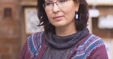 A portrait of Elena Opaleva wearing glasses and a purple cardigan.
