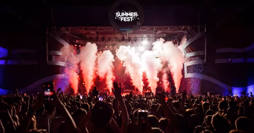 A large crowd at the Summer Fest music festival with stage lights and smoke effects.