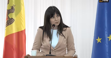 Victoria Belous speaking at a podium with Moldovan and EU flags in the background.