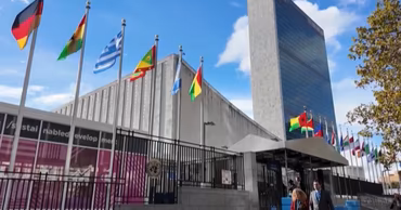 The United Nations headquarters building in New York with various national flags flying outside.