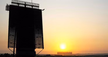 A silhouette of a large military radar installation against a sunset sky.