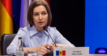 Maia Sandu sitting at a table with a nameplate and Moldovan flag.