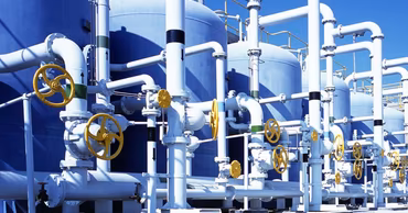 Industrial water treatment facility with large blue tanks and white pipes.