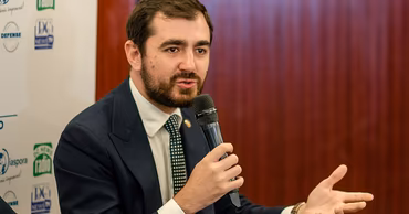 Claudiu Năsui speaking into a microphone at a press event.