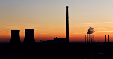 Silhouette of industrial factory chimneys and cooling towers against a sunset sky.