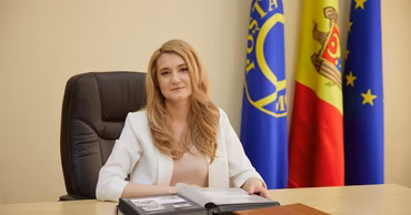 Violeta Cojocaru sitting at a desk with Posta Moldovei, Moldovan, and EU flags in the background.