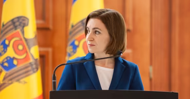 President Maia Sandu speaking at a podium with Moldovan flags in the background.
