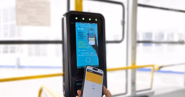 A hand using a smartphone to pay at an electronic ticket validator inside a public transport vehicle.