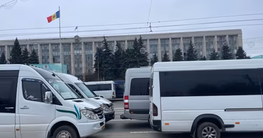 Several white passenger minibuses parked in front of a government building in Moldova.