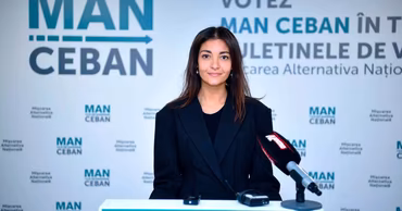 Olga Ursu standing at a podium with MAN party branding in the background.