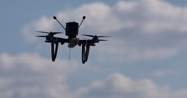 A small quadcopter drone flying against a cloudy blue sky.