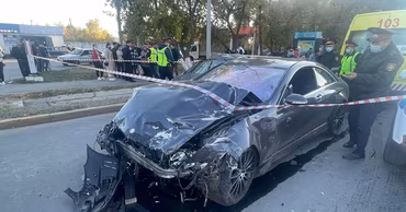 A heavily damaged Mercedes car at an accident scene with police officers and an ambulance.