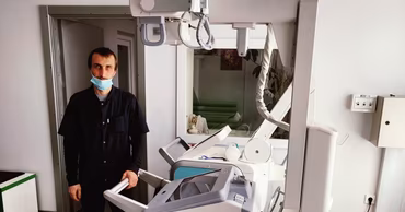 A medical professional standing next to a mobile X-ray machine in a clinical setting.