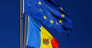 Flags of the European Union and Moldova waving against a clear blue sky.