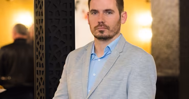 A portrait of Pavel Movila wearing a light grey blazer and blue shirt.