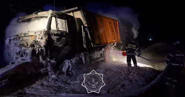 Firefighters extinguishing a burning truck at night in an industrial area.