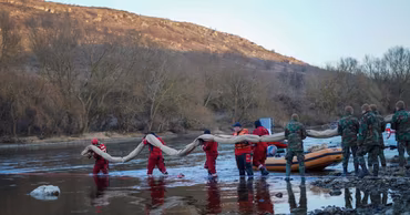 Emergency workers and soldiers deploying equipment in the Dniester river near a rocky bank.