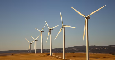 A row of wind turbines in a field under a clear blue sky.