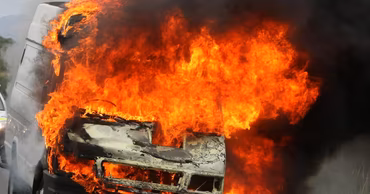 A white truck engulfed in intense flames and thick black smoke.