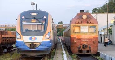 A modern Moldovan train next to an older locomotive at a railway station.