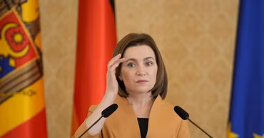 Moldovan President Maia Sandu speaking at a podium with flags in the background.