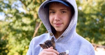 A young boy in a grey hoodie holding a small kitten.