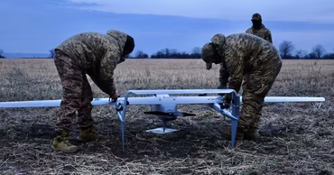 Military personnel in camouflage uniforms inspecting a drone in an open field.