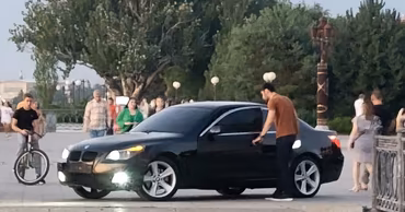 A black BMW car parked in a pedestrian area with people walking nearby.