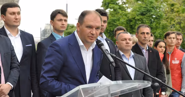 Ion Ceban speaking at a podium surrounded by people.