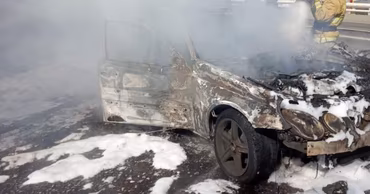 A firefighter extinguishing a burning car covered in foam.