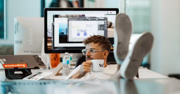 A freelancer sitting at a desk with a computer, holding a mug, representing independent work.