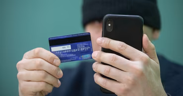 A person holding a smartphone and a bank card, representing financial fraud.